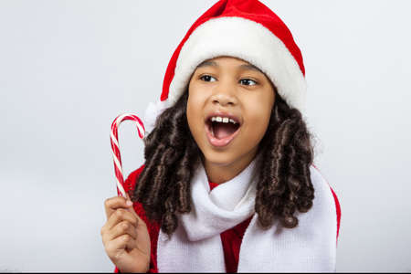 girl with a New Year gift. Joyful girl in a cap of Santa Claus with candyの写真素材