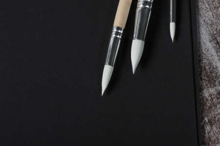 Art album and watercolor paint with paint brushes. View from above. empty blank black paper for...