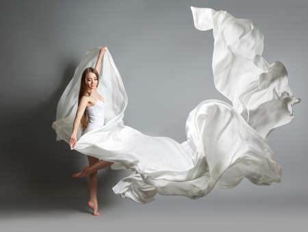 beautiful young girl dancing. The girl in flying white dress. A white cloth is flying in the air. White light dressの写真素材