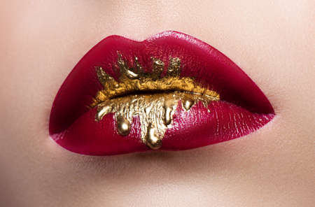 Beautiful female lips closeup. Red lipstick, gold paint flowing over his lips. Stock Photo Cosmetic Advertisingの写真素材