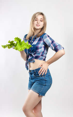 Young happy woman holding fresh green lettuce. Girl dressed in a shirt and denim shorts. Nutrition, diet, weight lossの写真素材