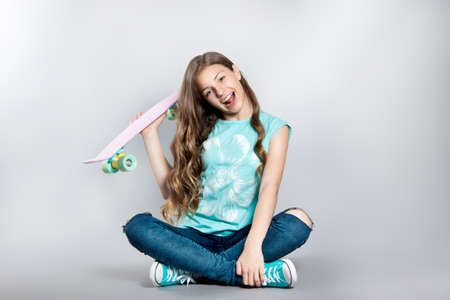 Girl posing with skateboard sitting in the studio. Joy, smile, positive emotions. Stock photos on a gray backgroundの写真素材