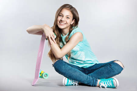 Girl posing with skateboard sitting in the studio. Joy, smile, positive emotions. Stock photos on a gray backgroundの写真素材