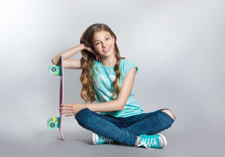 Girl posing with skateboard sitting in the studio. Joy, smile, positive emotions. Stock photos on a gray backgroundの写真素材