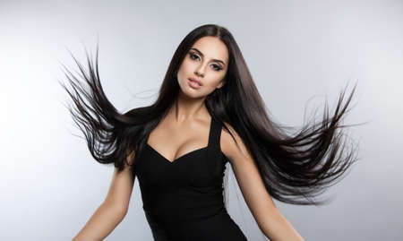Beautiful model with smooth flying hair. fashion portrait of a brunette woman in a black dressの写真素材