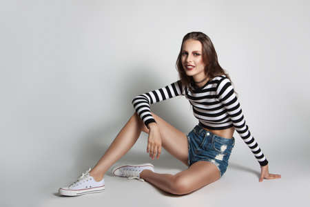 Pretty young girl in shorts and sweater striped posing in the studio. Beauty fashion photos. Model...
