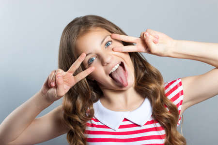 Closeup portrait young attractive girl with v fingers across the face move, isolated grey background. Positive human emotions, face expressionsの写真素材