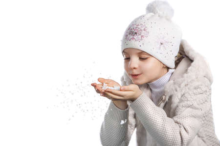 cute little girl in warm clothes on white background. Funny girl in winter hat blows off snowflakes with palmsの写真素材