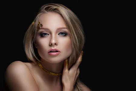 beautiful blonde with golden make-up. Beauty fashion. Face close-up portrait on a dark background.の写真素材