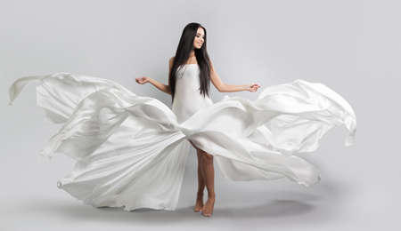 beautiful young girl in flying white dress. Flowing fabric. Light white cloth flying in the windの写真素材