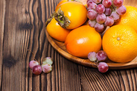 Persimmon. Orange. Grapes. Ripe, sweet fruit on a wooden table. Beautiful still lifeの写真素材
