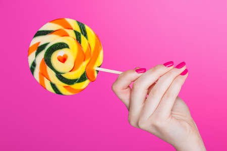 hand holding Colorful spiral lollipops. Isolation on a pink backgroundの写真素材