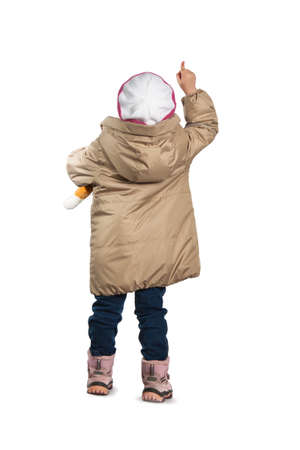a little girl standing with his back pointing her finger. Girl in winter clothes on a white background.の写真素材