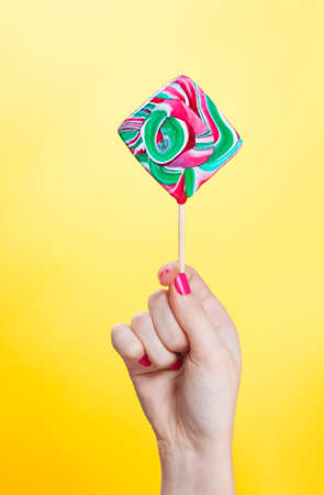 hand holding Colorful spiral lollipops. Isolation on a yellow backgroundの写真素材