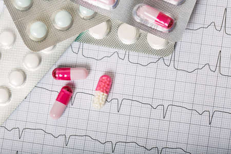 Pile of medical pills and pills on the background of the cardiac rhythm. cardiogramの写真素材