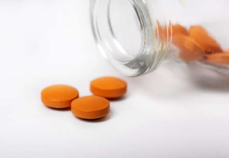 Orange pills medicine in bottle. An open vial with dropped pills on a light backgroundの写真素材