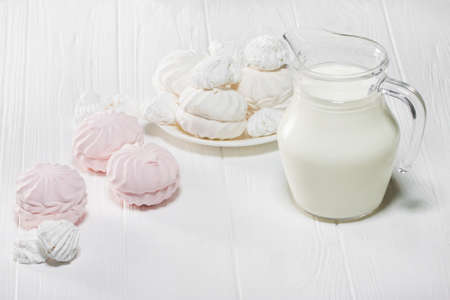 White and pink marshmallows and a jug of milk on a white wooden table. Beautiful light background.の写真素材