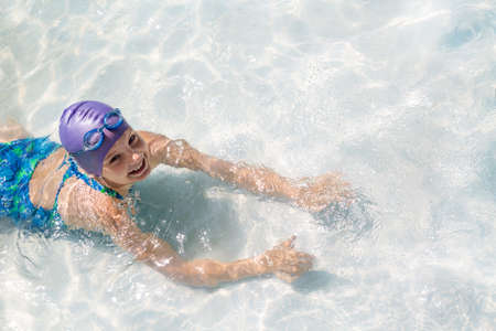 Joyful girl in a swimsuit and a cap floating in the poolの写真素材