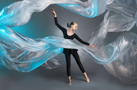 Girl in black clothes in the studio on the background of flying polyethylene film. Air flying film,...