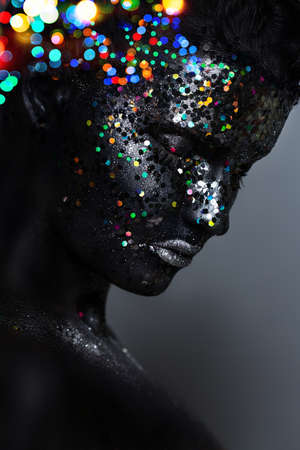 creative female portrait. face in black paint with large sequins. Dark backgroundの写真素材