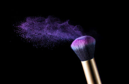 Cosmetics makeup brush and powder dust explosion. Isolation on a black background.