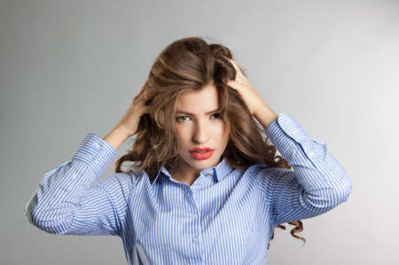 Young girl with beautiful long hair posing in the Studio. Girl holding hair. Blue shirt, grey backgroundの写真素材