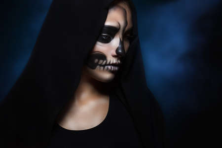 Halloween portrait of young beautiful girl in a black hood. skeleton makeup half faceの写真素材