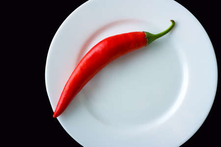 Red hot pepper on a white plate on a black background. Horizontal top view
