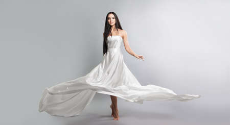 fashion photo of young girl in white dress flying tissue. Lightweight material. Grey backgroundの写真素材