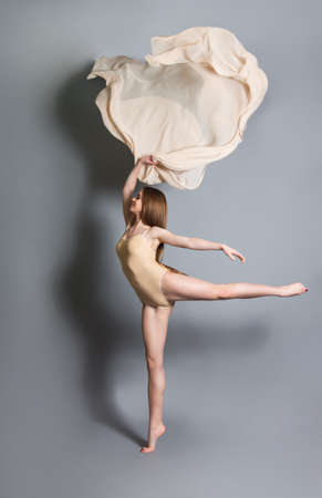 beautiful young girl dancing with cloth. Flying fluttering fabric. Gray background. vertical photoの写真素材