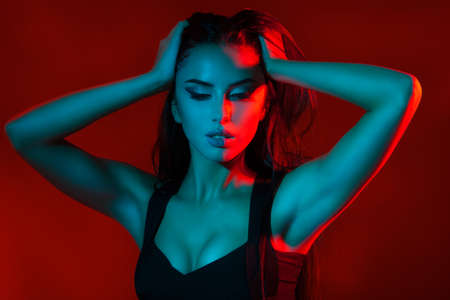 Studio creative portrait of beautiful girl model. Brunette in red and blue light of. Girl holding her headの写真素材