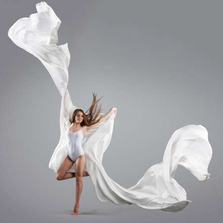 Young attractive girl dancing in the Studio with a white cloth. Fabric flies through the air. Model in white combidressの写真素材