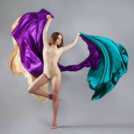 beautiful young girl dancing. Flowing fabric. The girl throws a colorful fabric. Fabric is flying. gray backgroundの写真素材