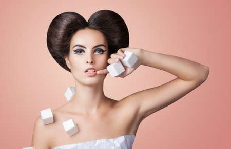 young beautiful model in a paper dress with voluminous cubes . creative makeup and hairstyle. pink background. Girl holding in hands white cubesの写真素材