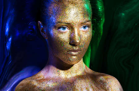 beautiful girl face, painted with gold paint with glitter. Close-up portrait on a black background....