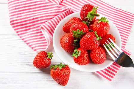 Fresh ripe strawberries on a plate. White wooden table, napkin in red and white stripes.の写真素材