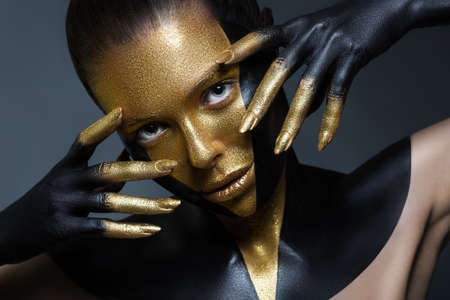Girl with gold and black paint on her face and body. Isolation on a black background in the Studio. Close-up face. Fingers in paint near the headの写真素材