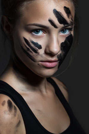 portrait of a young girl closeup. Face smeared with black paint. Beautiful blue eyesの写真素材
