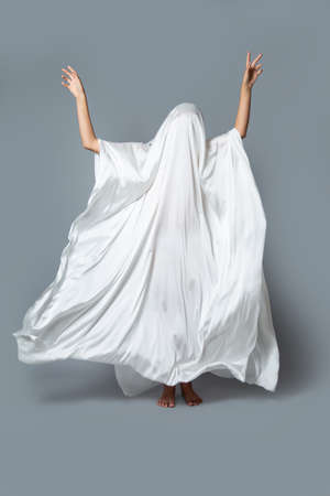 A girl in a Ghost costume on a gray background in the Studio. Halloween minimal concept.の写真素材