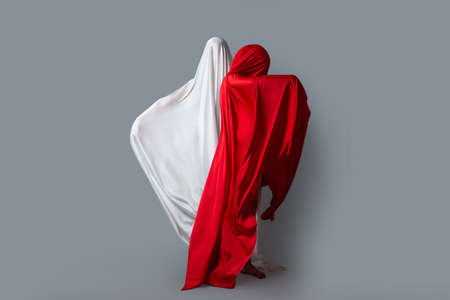 Female figures in fluttering in the wind fabrics. Red and white silhouette on grey background. Minimalism. Conceptの写真素材