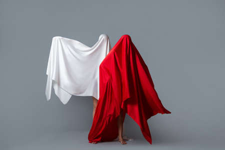 Female figures in fluttering in the wind fabrics. Red and white silhouette on grey background. Minimalism. Conceptの写真素材