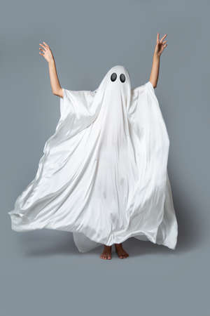 A girl in a Ghost costume on a gray background in the Studio. Halloween minimal concept.の写真素材