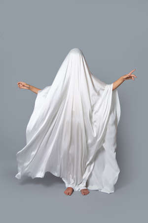 A girl in a Ghost costume on a gray background in the Studio. Halloween minimal concept.の写真素材
