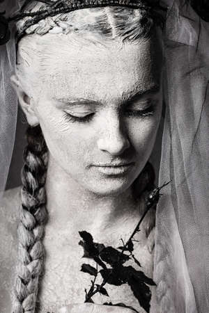 Artistic portrait of a girl covered in cracked white paint. Halloween makeup. Black and white veil,...