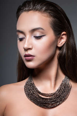 Beauty fashion portrait of a young beautiful girl posing in the Studio. Bright evening makeup close-up face. massive decoration on the neck. Open shouldersの写真素材