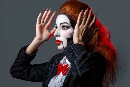Red-haired girl with creative make-up and hairstyle for a Halloween party. Hands raised. the image of a scary dollの写真素材