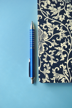 Floral notebook and a blue silver pen on blue flat layの写真素材