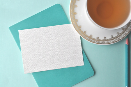 White fine china cup of tea with a blank note card and teal book on mint backgroundの写真素材