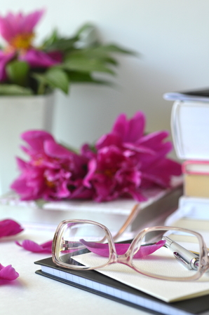 Bold violet pink peonies with blush pink glasses on a desk. Elegant feminine styled desktop workspace.Concept of working from home and studying.の写真素材