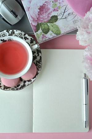 Elegant styled feminine desktop - relaxation, reading, creative writing, learning and journaling concept - with pink peonies, fruit tea and stylish stationeryの写真素材